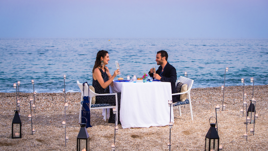 A couple dines at a romantic candle-lit table on a beach, overlooking the sea at Banyan Tree Tamouda Bay.